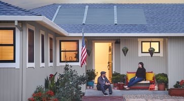 House with solar shingles on roof, two people sitting in front of the house
