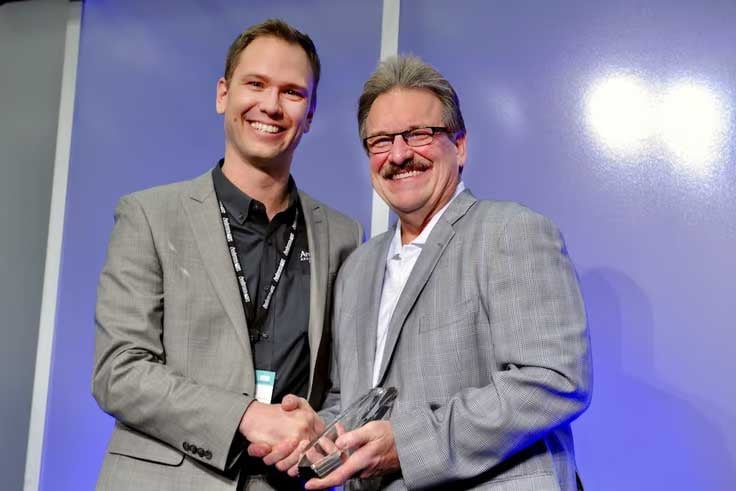 Two men smiling, shaking hands, holding an award